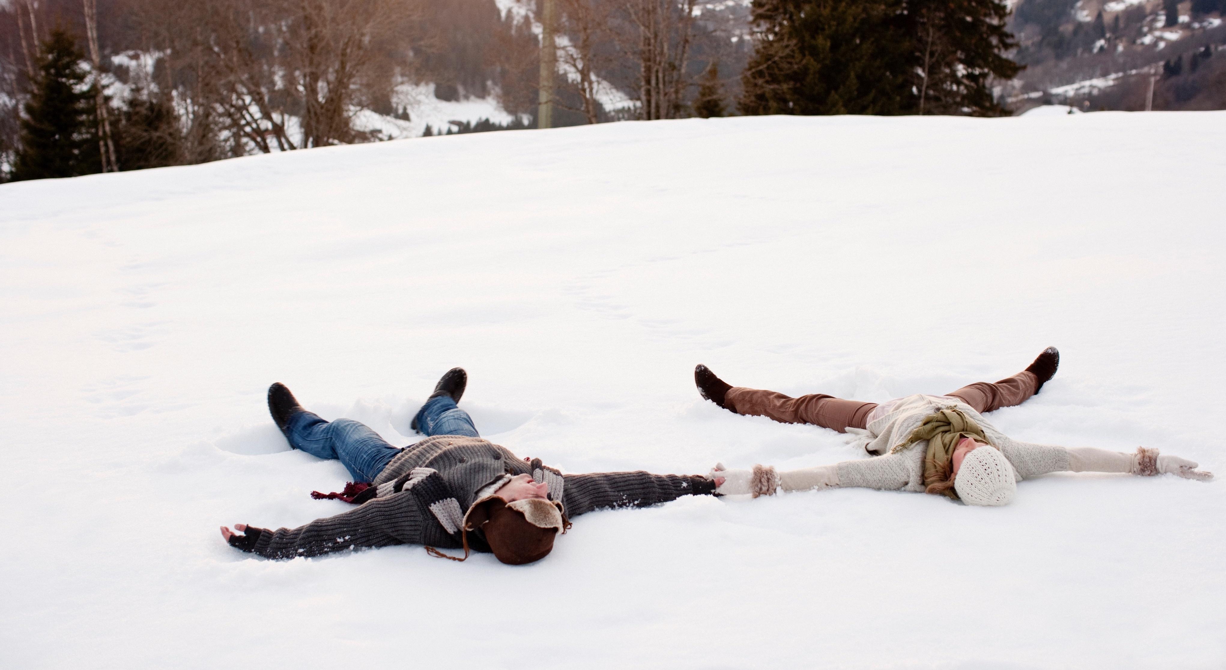 A couple makes snow angels together.