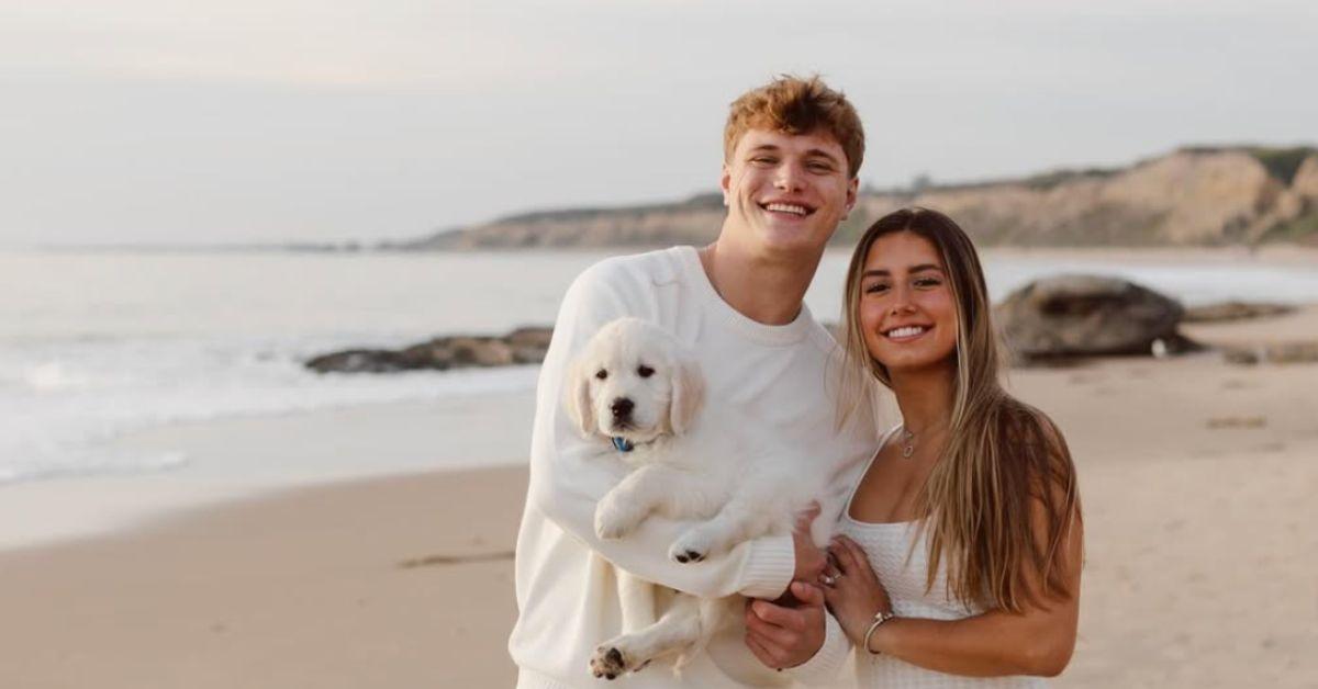 Katya Kuropas and J.J. McCarthy holding a dog on a beach. 